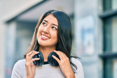 Genç İspanyol kadın gülümseyerek şehirde kulaklık takarak müzik dinliyor..