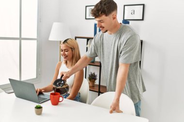 Kadın evde dizüstü bilgisayar kullanıyor ve erkek arkadaşı kahve dolduruyor..