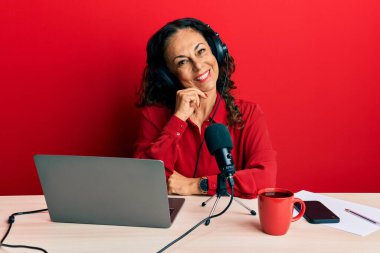 Radyo stüdyosunda çalışan orta yaşlı güzel bir kadın kameraya kollarını kavuşturup gülümseyerek ve çenesini kaldırarak bakıyor. Olumlu düşünmek. 