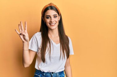 Güzel esmer, beyaz tişört giyen genç bir kadın dört numarayı gösterip işaret ederken kendinden emin ve mutlu bir şekilde gülümsüyor.. 