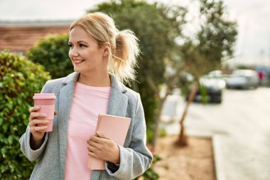 Genç sarışın iş kadını gülümseyerek şehirde kahve içiyor..