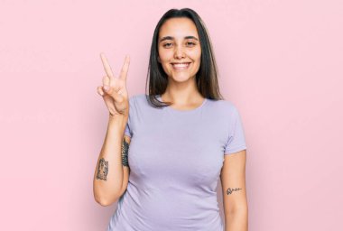 Gündelik kıyafetler giyen, gülümseyen, kameraya göz kırpan genç İspanyol kadın zafer işareti yapıyor. İki numara.. 