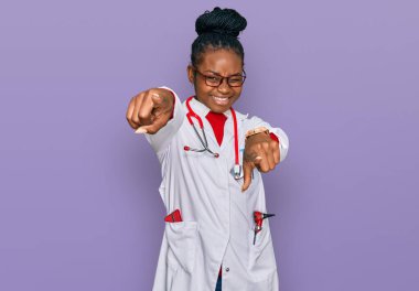 Genç Afro-Amerikan kadın doktor üniforması ve steteskop takmış parmaklarıyla sizi ve kamerayı işaret ediyor. 