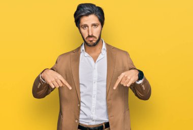 İş kıyafetleri giymiş genç İspanyol adam üzgün ve üzgün görünüyor, parmaklarıyla yön gösteriyor, mutsuz ve depresif.. 