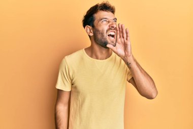 Sarı arka planda sıradan sarı tişörtler giyen sakallı yakışıklı bir adam el ele tutuşup bağırıyor. iletişim konsepti. 