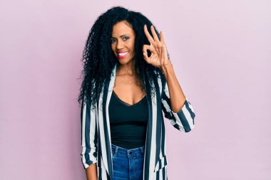 Orta yaşlı Afro-Amerikalı kadın, günlük kıyafetler giyip gülümsüyor ve el ve parmaklarıyla 