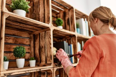 Orta yaşlı kadın evde toz bezi kullanırken mutlu bir şekilde gülümsüyor..