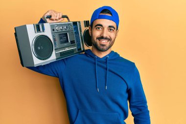 Kasetçalar tutan genç İspanyol adam, pozitif ve mutlu görünerek müzik dinliyor ve kendine güvenen bir gülümsemeyle dişlerini gösteriyor. 