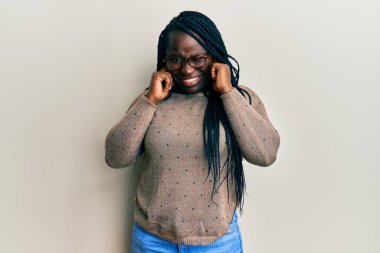 Gürültülü müzik sesi için saçı örgülü, gözlüklü, kulakları parmaklarıyla kulakları kulaklarla kaplı genç siyahi bir kadın. sağır kavramı. 