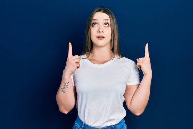 Gündelik beyaz tişört giyen genç İspanyol kız hayret ve şaşkınlık içinde yukarı baktı ve parmaklarıyla işaret etti ve kollarını kaldırdı.. 