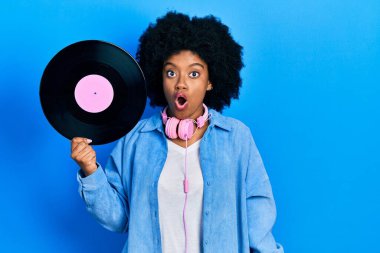 Kulaklık takan Afro-Amerikalı genç bir kadın. Elinde vinil disk var. Korkmuş ve ağzı açık bir şekilde hayrete düşmüş. 