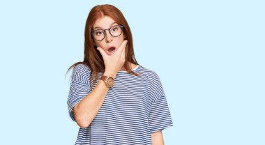 Gündelik giysiler ve gözlük takan genç bir kadın inançsızlıktan, şaşkınlıktan ve elleri çenesinde olan hayret verici bir ifadeden etkilenmiş görünüyor. 