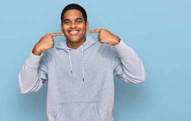 Gündelik kazak giyen, neşeli gülümseyen ve parmaklarıyla ve ağzıyla işaret eden genç, yakışıklı İspanyol bir adam. diş sağlığı kavramı. 