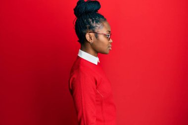 Afro-Amerikalı genç bir kadın günlük kıyafetler ve gözlük takıyor. Yan tarafa bakıyor, rahat poz veriyor, kendine güvenen bir gülümsemesi var.. 