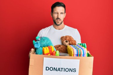 Elinde oyuncaklarla bağış kutusu tutan yakışıklı genç adam kameraya seksi bir ifadeyle bakıyor, neşeli ve mutlu bir yüz.. 