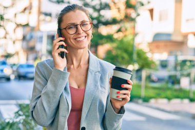 Sarışın iş kadını akıllı telefondan konuşuyor ve şehirde kahve içiyor..