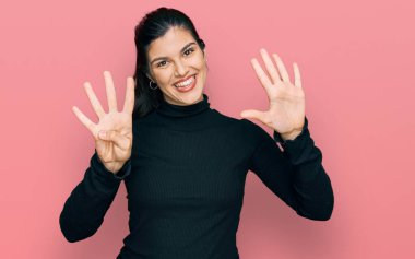 Gündelik kıyafetler giyen genç İspanyol kadın dokuz numarayı gösterip işaret ederken kendinden emin ve mutlu bir şekilde gülümsüyor.. 