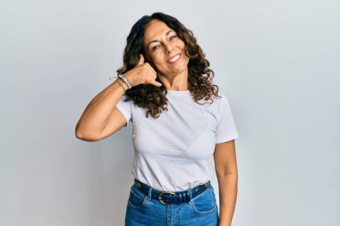 Orta yaşlı İspanyol kadın, günlük beyaz tişörtler giyip gülümsüyor telefonla el ve parmaklarıyla jest yapıyor telefonda konuşuyor gibi. iletişim kavramları. 