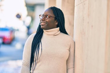 Genç Afrikalı Amerikalı kadın gülümseyerek şehirde mutlu mesut duruyor..