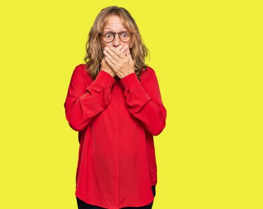 Kırmızı arka plan üzerine gündelik tişört giyen orta yaşlı sarışın kadın yanlışlıkla elleriyle ağzını kapatırken şok oldu. gizli kavram. 