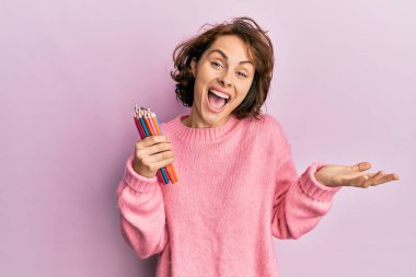 Genç esmer kadın elinde renkli kalemlerle başarıyı mutlu bir gülümsemeyle kutluyor ve kazanan el kaldırarak ifade ediyor. 