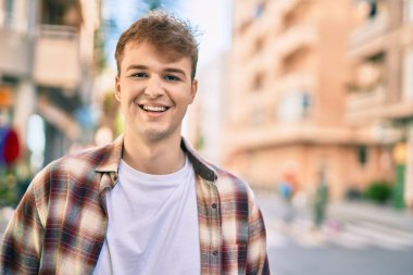 Genç beyaz adam gülümseyerek şehirde mutlu mesut duruyor..