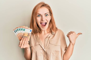 Elinde 50 avroluk banknotlar tutan beyaz bir kadın başparmağıyla yan tarafa bakıp ağzı açık gülümsüyor. 