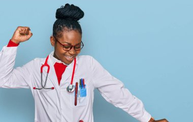 Genç Afro-Amerikan kadın doktor üniforması giyiyor ve steteskop dansı yapıyor mutlu ve neşeli, hareketli ve kendinden emin müzik dinliyor. 