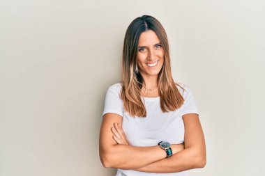 Esmer, beyaz tişörtlü mutlu yüzlü, kolları çapraz bir şekilde kameraya bakan genç bir kadın. pozitif kişi. 