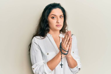 Güzel İspanyol kadın Katolik tespihi ile oynuyor cahil ve kafası karışık bir ifade. şüphe kavramı. 