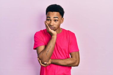 Genç Afro-Amerikalı adam Casua tişörtü giyip kollarını kavuşturarak depresyondan sıkılmış ve yorgun göründüğünü düşünüyor.. 