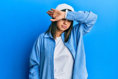 Tatlı yün şapkalı, kollarıyla gözlerini kapatan genç Latin kadın ciddi ve üzgün görünüyor. Görme, saklama ve reddetme konsepti 