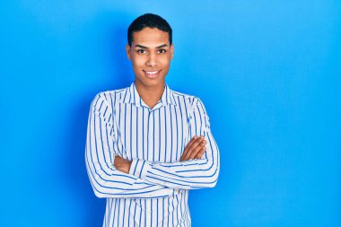 Sıradan kıyafetler giyen, kollarını kavuşturup kameraya gülümseyen Afro-Amerikan genç adam. pozitif kişi. 