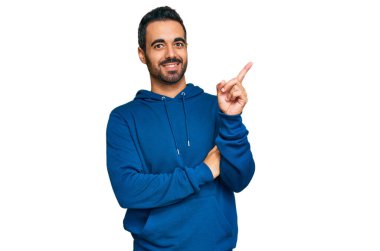 Gündelik kıyafetler giyen genç İspanyol adam gülümsüyor mutlu bir şekilde elini ve parmağını yana uzatıyordu. 