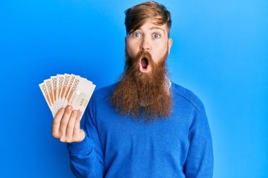 Genç İrlandalı kızıl saçlı adam elinde 5000 Güney Koreli para kazandı. Korkmuş ve ağzı açık kalmış, şaşırmış, inançsız bir yüz. 