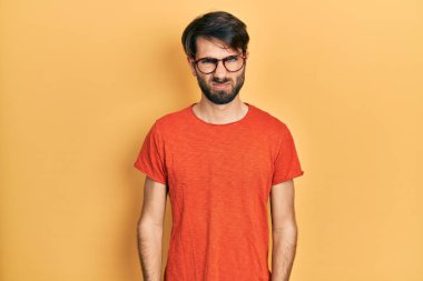 Gündelik kıyafetler giyen, gözlüklü, şüpheci ve gergin genç İspanyol bir adam sorun yüzünden surat asıyor. negatif kişi. 