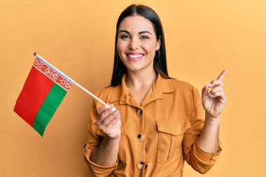 Genç esmer kadın elinde Belarus bayrağı tutarken mutlu bir şekilde gülümsüyor. 