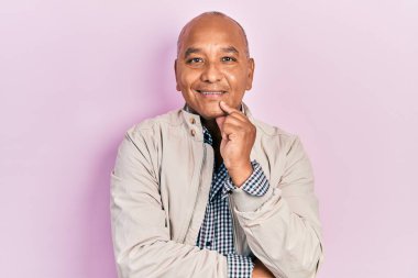 Orta yaşlı, sıradan kıyafetler giyen, kameraya gülümseyen kolları çapraz ve çenesi açık bakan Latin bir adam. Olumlu düşünmek. 