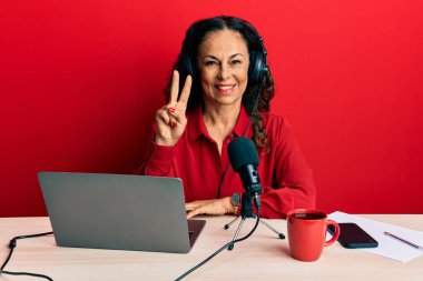 Radyo stüdyosunda çalışan orta yaşlı güzel bir kadın iki numarayı gösterip işaret ederken kendine güvenen ve mutlu bir şekilde gülümsüyor.. 