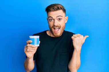 Kulak kiri temizleyicisi tutan genç kızıl saçlı adam baş parmağını yana kaldırıyor ve ağzı açık gülümsüyor. 