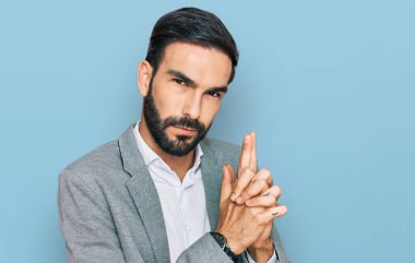 İş kıyafetleri giymiş genç İspanyol bir adam sembolik bir silahla el kol hareketi yapıyor, cinayet silahlarıyla oynuyor, sinirli bir yüz ifadesi var. 