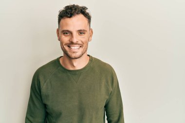 Yüzünde mutlu ve havalı bir gülümseme olan sıradan kıyafetler giyen genç İspanyol bir adam. şanslı kişi. 