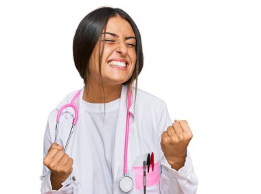 Güzel İspanyol kadın doktor üniforması giyiyor ve steteskop çok mutlu ve heyecanlı kollarını kaldırıp, gülümseyerek ve başarı için bağırarak kazanan jestler yapıyor. kutlama konsepti. 