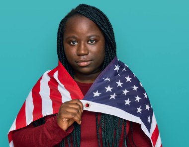 Birleşik Devletler bayrağı tutan siyah örgülü genç bir kadın. Düşünce tarzı ve ayık ifadesi. Kendine güvenen biri. 