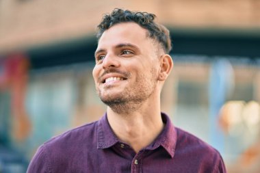 Genç İspanyol adam gülümseyerek şehirde mutlu mesut dikiliyor..