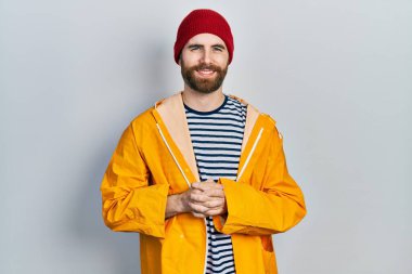 Sakallı, sarı yağmurluklu, elleri çapraz parmaklı, gevşemiş ve neşeli gülümseyen beyaz bir adam. Başarı ve iyimserlik 