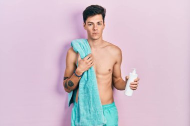 Genç İspanyol adam mayo giyiyor ve elinde güneş kremi tutuyor şüpheci ve gergin, sorun yüzünden surat asıyor. negatif kişi. 