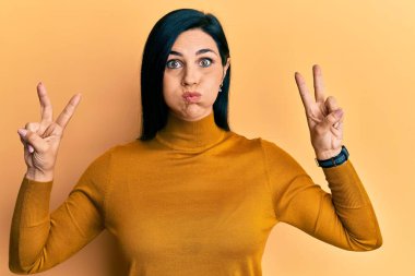 Kafkasyalı genç bir kadın zafer işareti yapıyor. Komik yüzlü, yanak şişiren pozitiflik işareti. Ağzı havayla şişer, havayı yakalar.. 