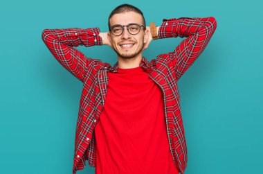 İspanyol genç adam günlük kıyafetler giyiyor rahatlıyor ve esniyor, kolları ve elleri başının arkasında mutlu bir şekilde gülümsüyor. 