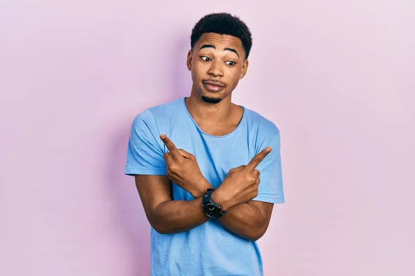若いアフリカ系アメリカ人の男を着てカジュアルブルーTシャツを指で両側を指して 異なる方向は反対 — ストック写真